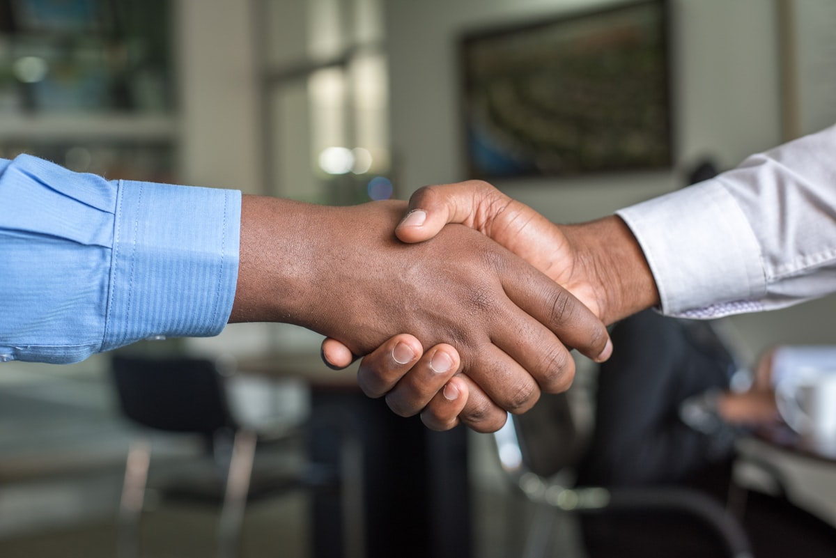 Two people shaking hands across a desk in an office.